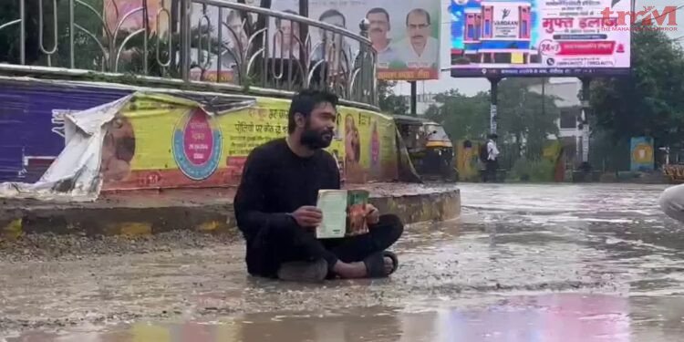 रीवा में युवक का अनोखा प्रदर्शन, किताब लेकर सड़क पर बरसते पानी में बैठा